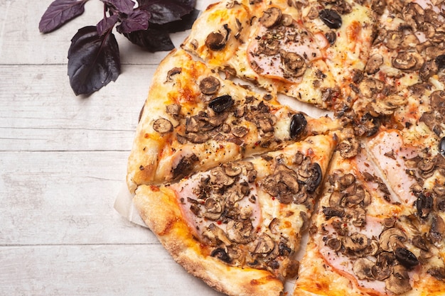 Pizza com presunto e cogumelos em uma mesa de madeira branca.