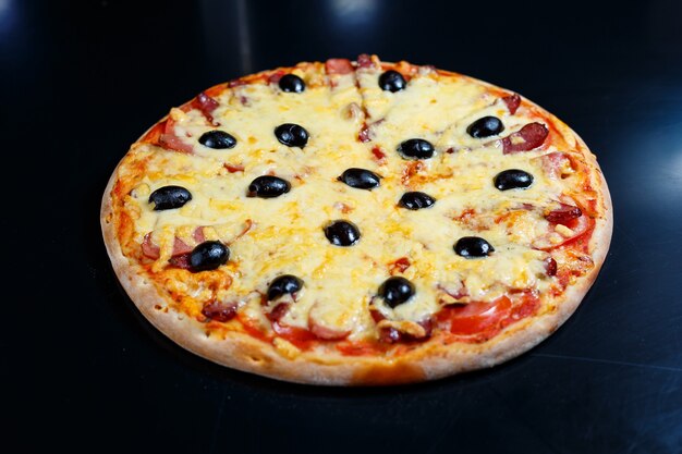 Pizza com queijo e molho de tomate, azeitonas, mussarela fresca, parmesão e manjericão e carne em fundo escuro