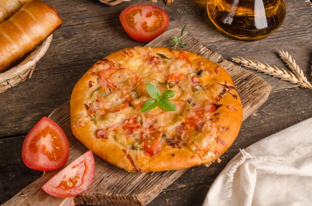 Pizza com queijo e tomate em um fundo de madeira com ingredientes, fast food