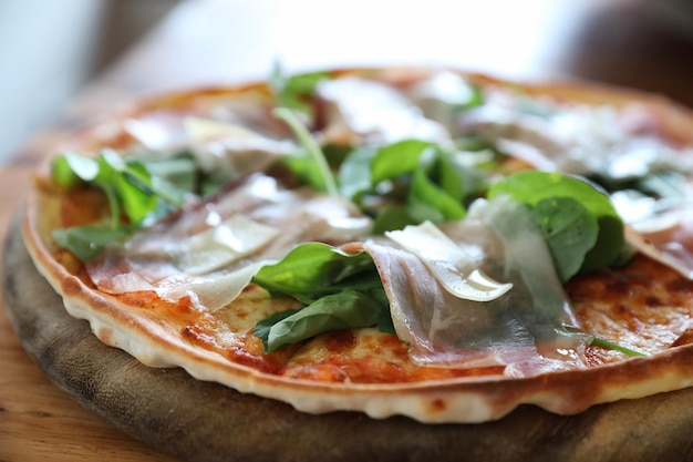 Pizza com rúcula de salada de presunto de parma em molho de tomate com fundo de mesa de madeira