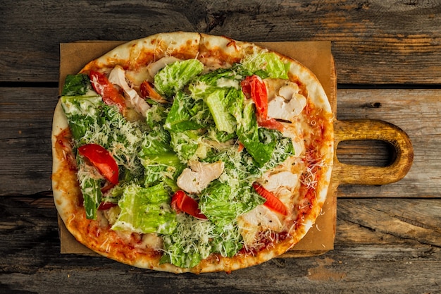 Pizza com salada césar. Carne de frango, tomate, alface, molho, queijo ralado, em tábua de madeira