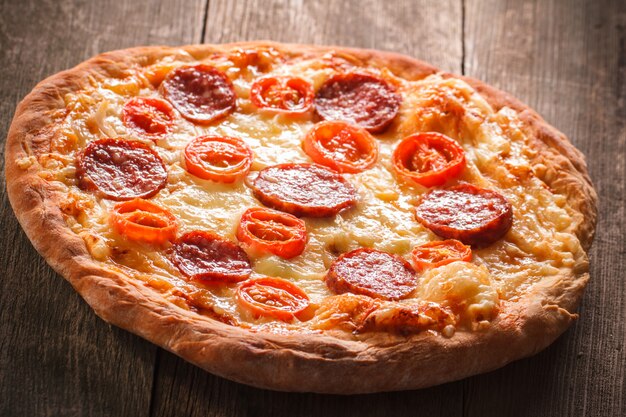 Pizza com salame e legumes em um fundo de madeira velho.