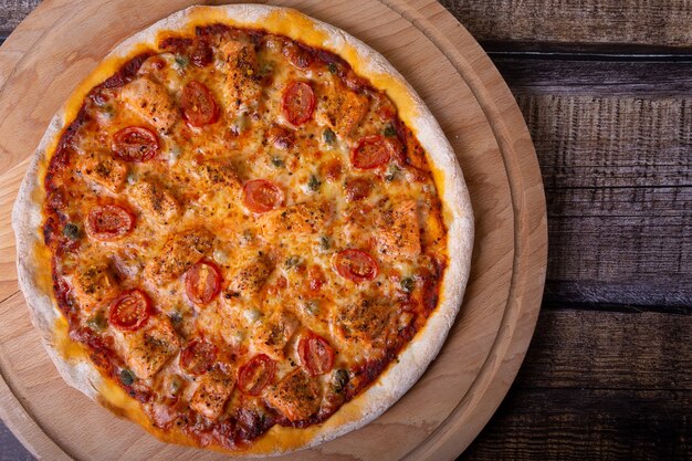 Pizza com salmão, tomate e alcaparras em uma placa de madeira. pizza inteira.