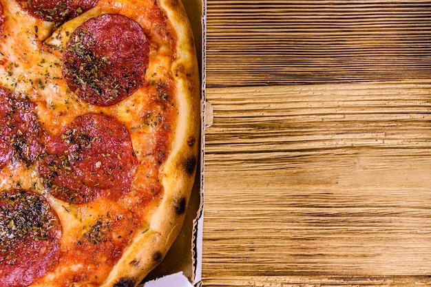 Pizza com salsicha de salame e queijo parmesão em caixa de papelão em uma mesa de madeira Vista superior