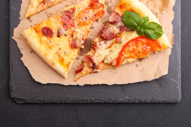 Pizza com salsicha, presunto, tomate e queijo, decorado com manjericão e cortado em pedaços em um pergaminho