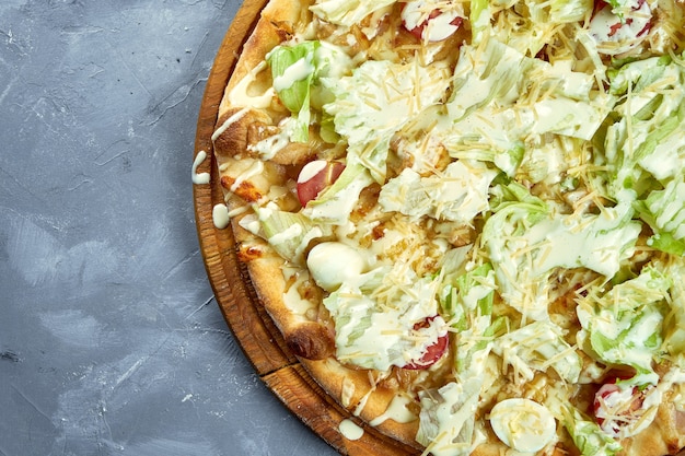 Pizza com tomate cereja, alface, parmesão e frango em um fundo cinza