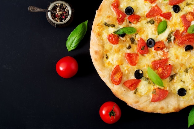 Foto pizza com tomate, mussarela, manjericão e azeitonas.