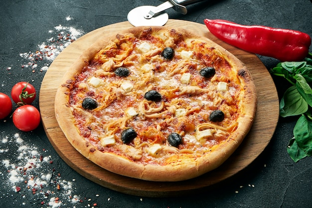 Pizza com um grande número de coberturas: frango, cebola, cogumelos, azeitona. Pizza em composição com ingredientes em uma mesa preta