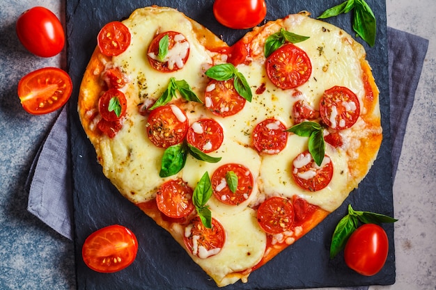 Pizza de corazón con mozzarella y tomates en pizarra