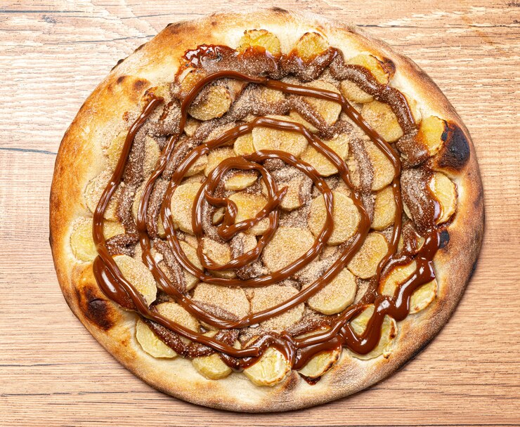 Foto pizza de banana com calda de chocolate e canela em pó, servida em mesa de madeira