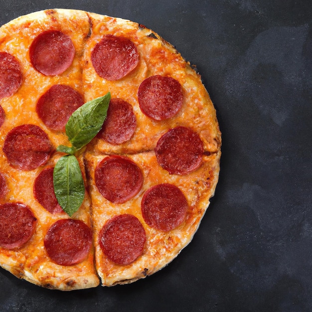 Pizza de calabresa saborosa e ingredientes de cozinha tomate manjericão em fundo de concreto preto Vista superior