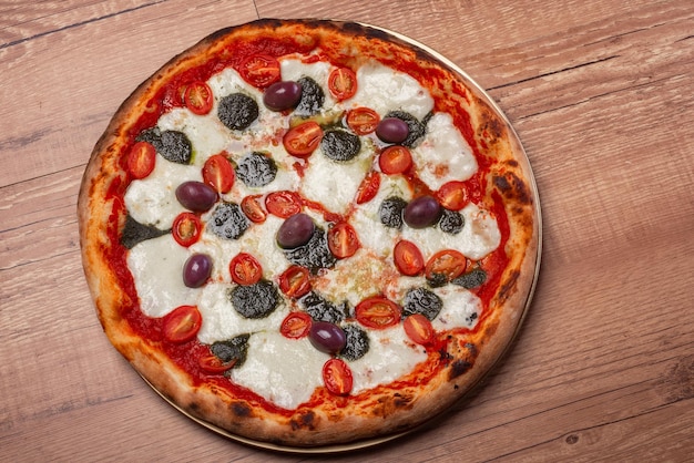 Pizza de mussarela de búfala com tomate cereja pesto de manjericão e azeitonas pretas na mesa de madeira rústica