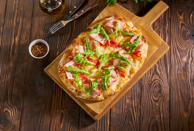 Pizza de pão sírio com presunto e rúcula em mesa de madeira escura