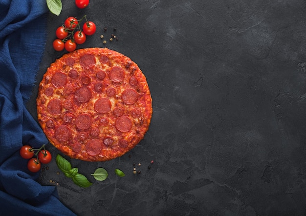 Pizza de Pepperoni quente e picante, assada e redonda fresca com tomates com manjericão no fundo da mesa de cozinha preta