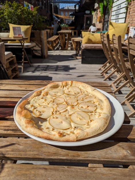 Foto pizza de pêra e queijo em um prato branco em um café de rua fica em uma mesa de madeira