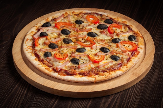 Pizza de presunto com pimentão e azeitonas em tábua de madeira na mesa