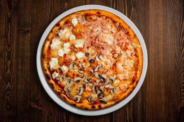 Pizza de presunto, peixe, cogumelos e queijo feta, fundo de madeira, chave baixa, vista superior