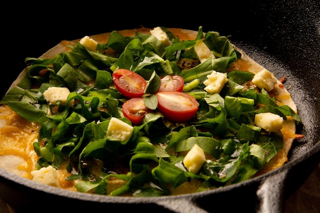 Pizza de rúcula com queijo e tomate cereja em frigideira de ferro fundido em vista frontal cortada