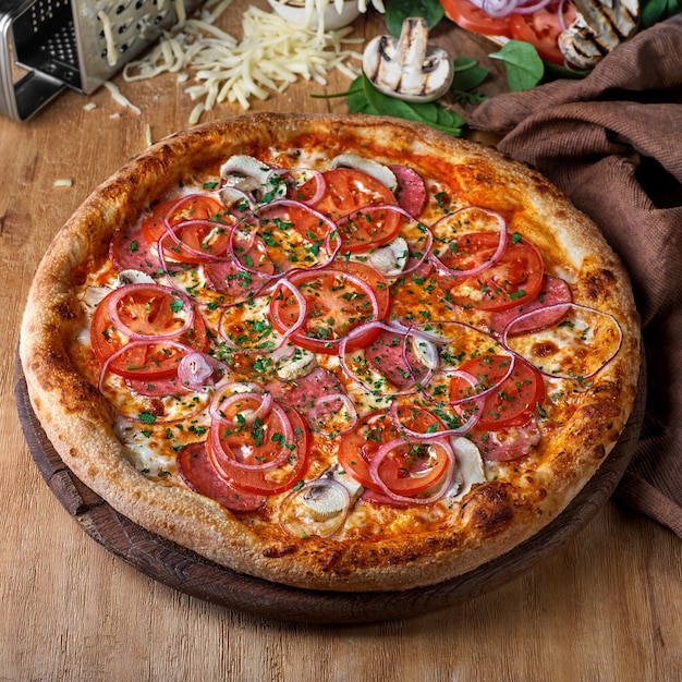 Pizza de salame inteiro fatiado e cogumelos com ingredientes em uma mesa de madeira