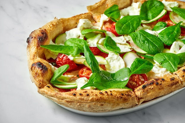 Pizza deliciosa com abobrinha, burrata, tomate seco e espinafre em prato branco sobre mármore branco