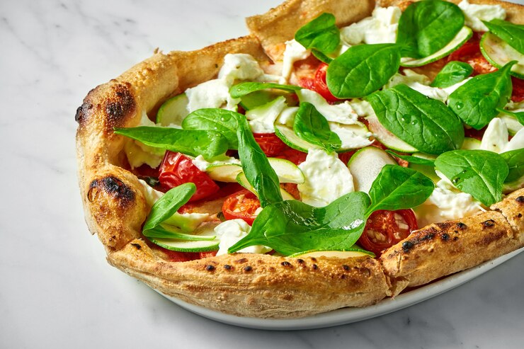 Foto pizza deliciosa com abobrinha, burrata, tomate seco e espinafre em prato branco sobre mármore branco