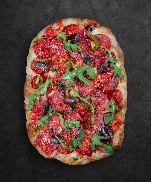 Pizza Diavolo mit Chorizo Rucola Jalapeno Chili Kalamata Pesto Römische Pizza rechteckig auf dunklem Hintergrund