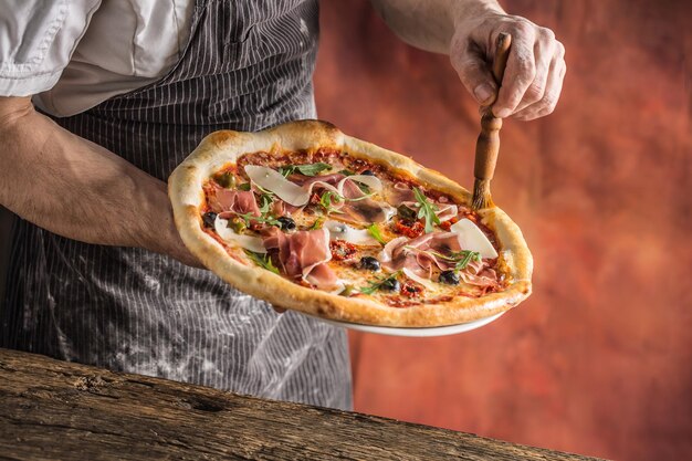 Pizza e Chef Chef no restaurante prepara uma pizza e decora-a com óleo de oliva