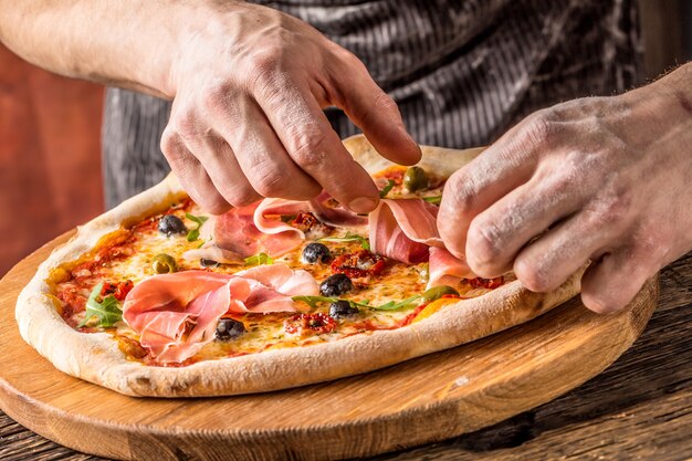 Pizza e Chef. O chef do restaurante prepara uma pizza e a decora com presunto