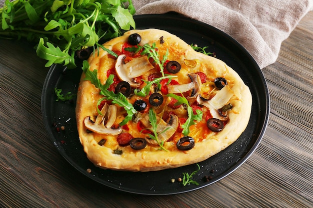 Pizza em forma de coração na bandeja de metal com fundo de madeira