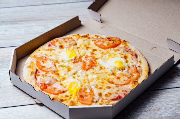 Pizza em uma caixa de papelão contra uma madeira cinza