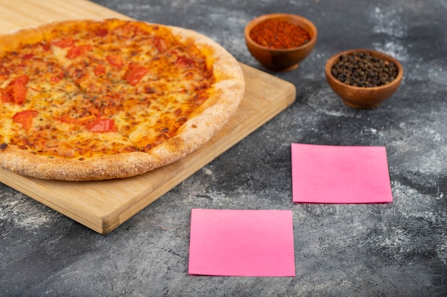 Pizza entera con especias y pegatinas colocadas sobre la mesa de piedra.
