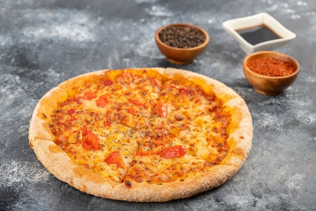 Pizza entera con especias y salsa de soja colocada sobre la mesa de piedra.