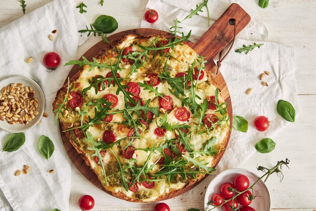 Foto pizza entera de pan plano con pesto y salmón cubierta con tomates y rúcula sobre una tabla