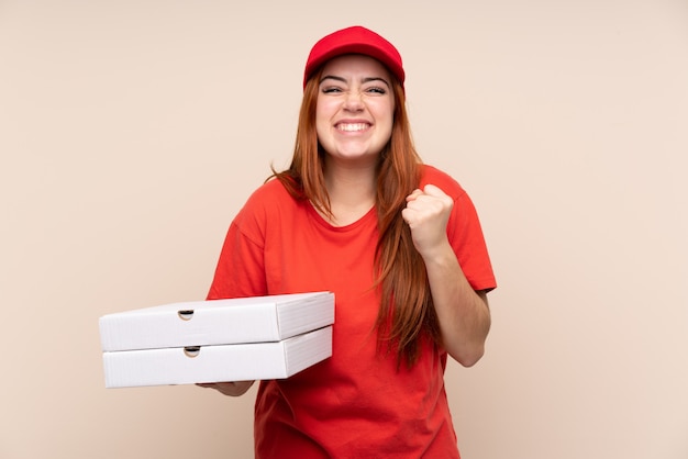 Pizza entrega adolescente menina segurando uma pizza sobre parede isolada comemorando uma vitória