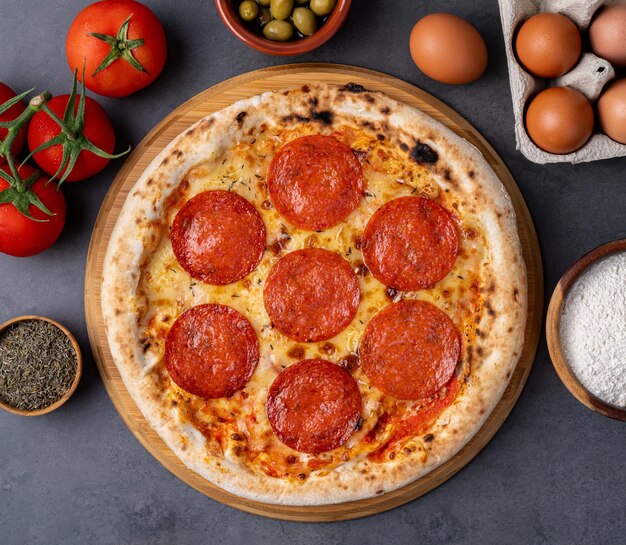 Pizza estilo salchicha de pepperoni sobre fondo de piedra con tomates, aceitunas y orégano