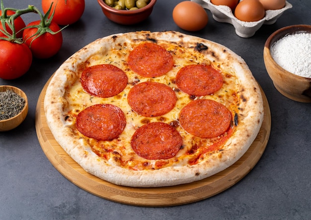Pizza estilo salchicha de pepperoni sobre fondo de piedra con tomates, aceitunas y orégano