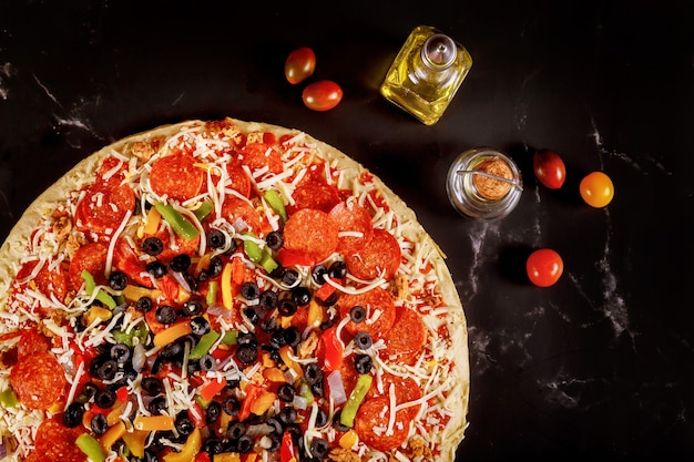 Pizza extra grande con aceitunas, pepperoni y tomates en negro.