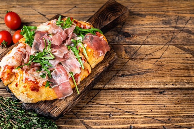 Pizza fatiada com presunto de parma, rúcula e queijo parmesão em uma placa de madeira. fundo de madeira. vista do topo. copie o espaço.