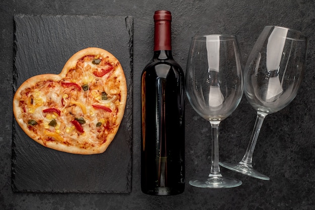 Pizza en forma de corazón para el día de San Valentín con una botella de vino y dos copas en pizarra