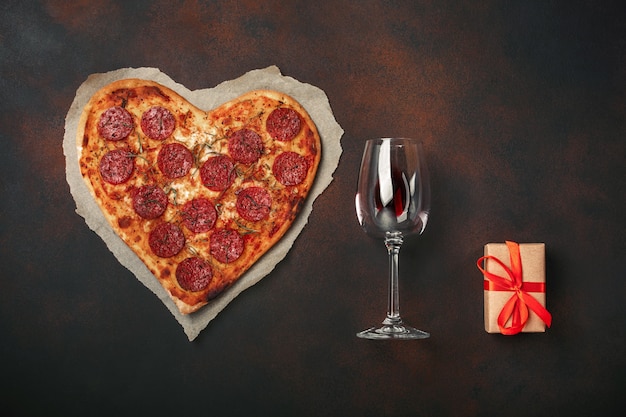 Pizza en forma de corazón con mozzarella, salteada, copa de vino, caja de regalo sobre fondo oxidado