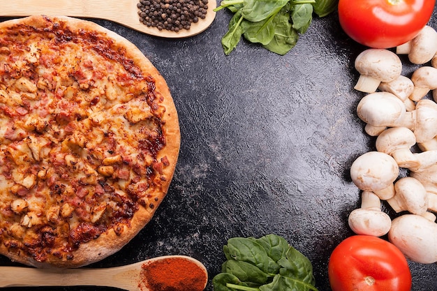 Pizza fresca ao lado de cogumelos, espinafre e tomate na mesa de madeira escura