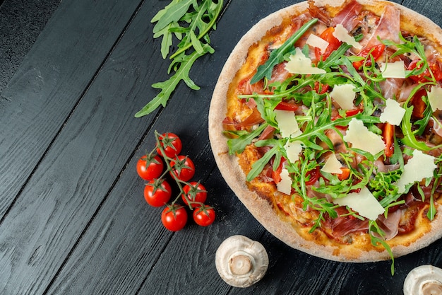 Pizza fresca casera con rúcula, parmesano y tomates cherry en una madera negra con espacio de copia.