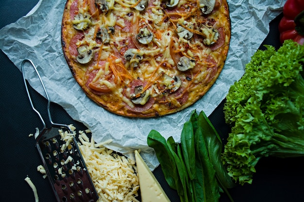 Pizza fresca com salsicha, tomate, cogumelos e queijo em uma superfície escura