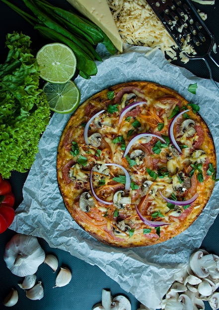 Pizza fresca com salsicha, tomate, cogumelos e queijo em uma superfície escura