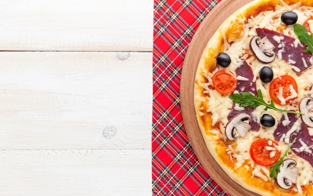 Foto pizza fresca em estilo rústico italiano com cogumelos de azeitonas espasmódicas e três tipos de queijo em um fundo claro de madeira