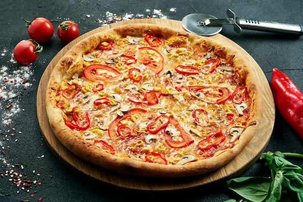 Pizza con una gran cantidad de ingredientes: cebollas, champiñones, queso, tomate y pimiento. Pizza en composición con ingredientes sobre una mesa negra. Comida vegetariana