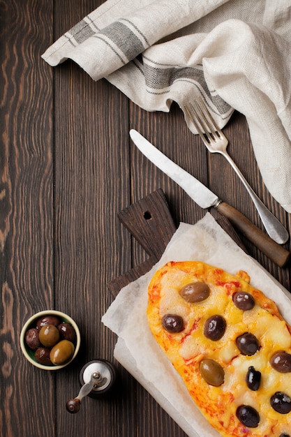 Pizza griega ovalada con aceitunas y tomate en rústico de madera oscura.