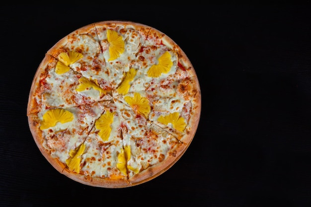 pizza hawaiana cubierta con piña en un fondo negro