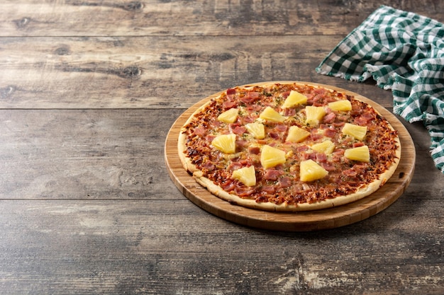 Pizza hawaiana con piña y queso sobre mesa de madera