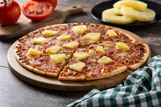 Foto pizza hawaiana con piña y queso sobre mesa de madera